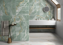 Carica l&#39;immagine nel visualizzatore di Gallery, Un bagno moderno è caratterizzato dalle piastrelle in marmo PAVIMENTO/RIVESTIMENTO 60X120 ELITE GREEN di Selvaggio Edilpref S.R.L., da un lavabo galleggiante bianco, da uno specchio rotondo, da una panca in legno, da un portasciugamani nero e da un&#39;ampia finestra che riempie lo spazio di luce.